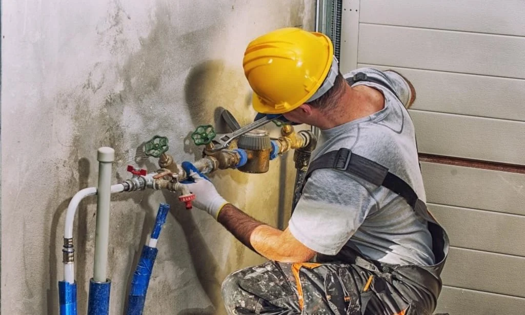 Plumber in a hard hat repairing a main water shut-off valve, plumbing service in Mississauga