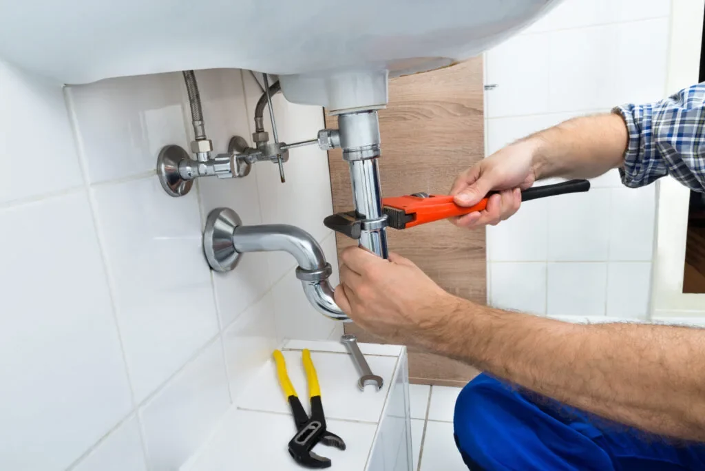 Plumber repairing a bathroom sink drain with a pipe wrench, plumbing service in North York