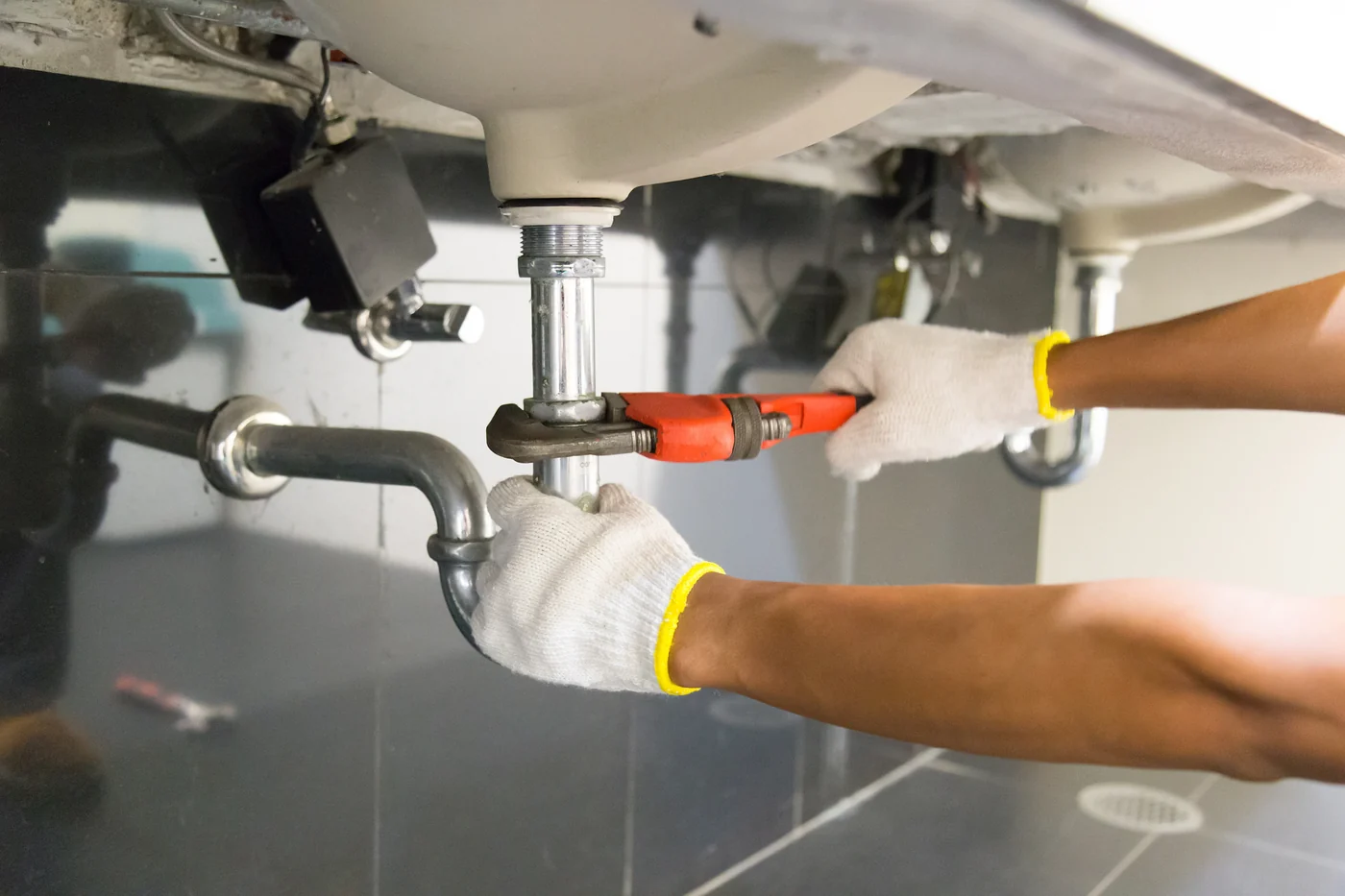 Plumber tightening a chrome sink drain with a red pipe wrench, plumbing repair in Toronto, Ontario