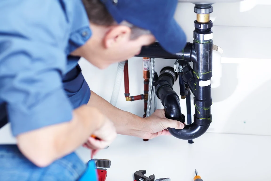 Licensed plumber connecting a black ABS P-trap under a sink, plumbing services in Toronto