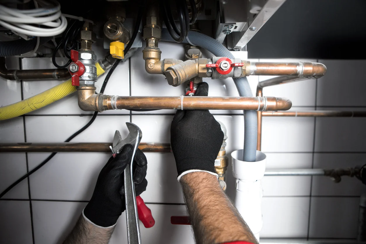 Plumber adjusting copper water lines with a wrench under a wall-mounted boiler